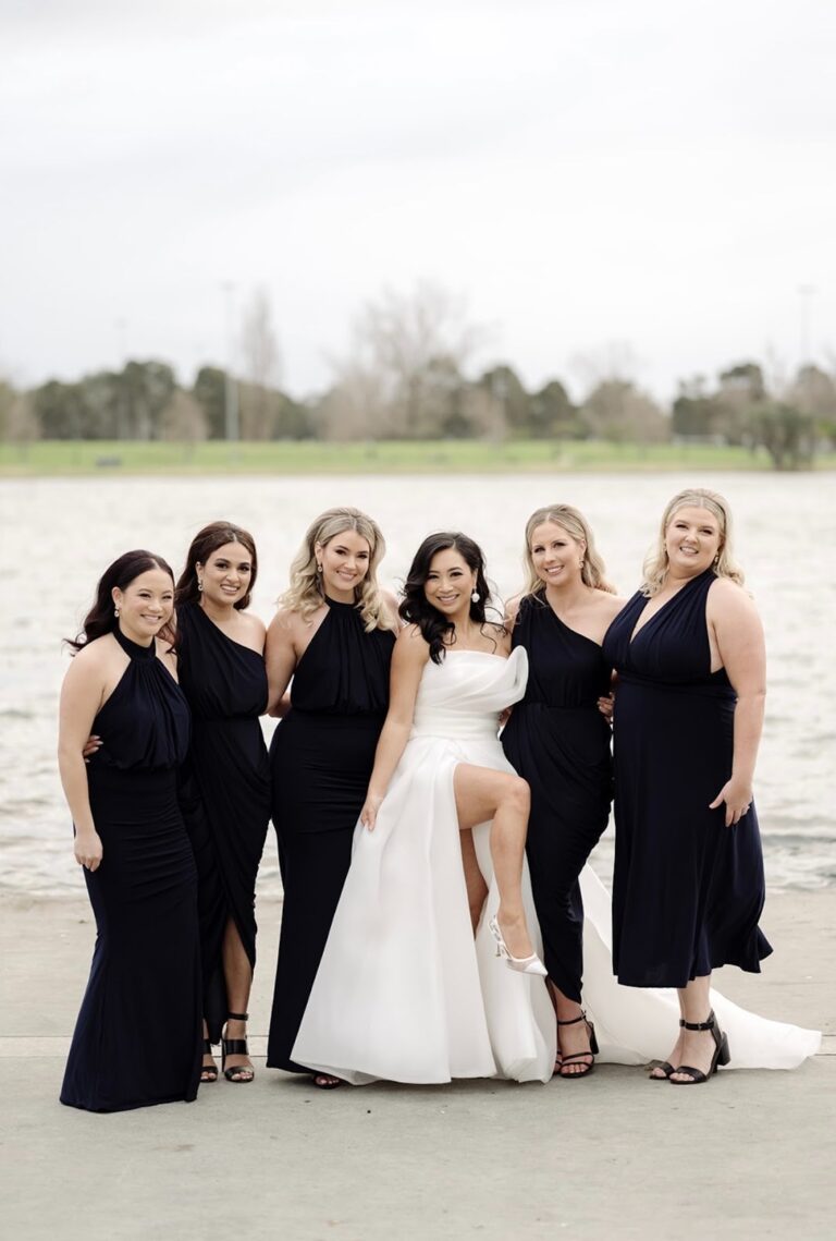 Bride with her bridesmaids in black gowns beside the water