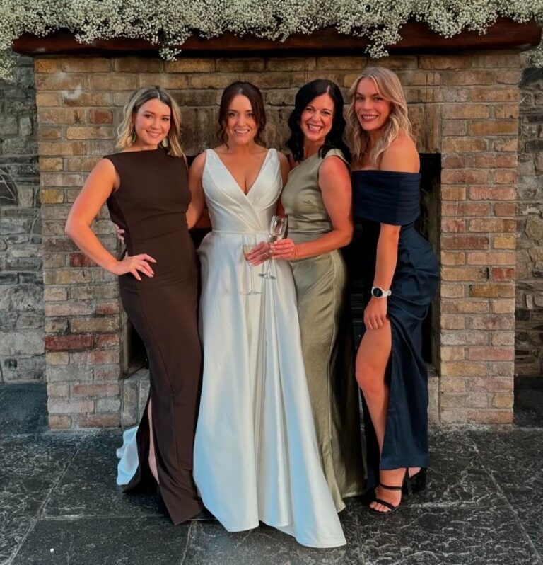 Bride in an ivory gown with three wedding guests in front of a stone wall