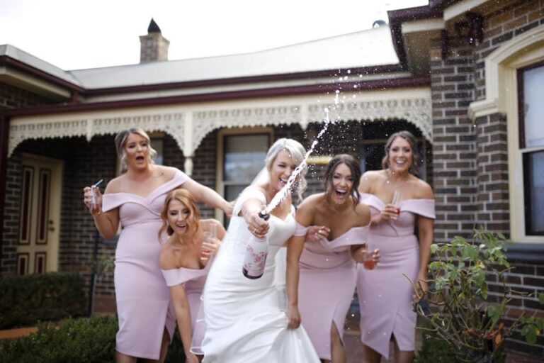 Bride celebrating with her bridesmaids in blush dresses as champagne sprays
