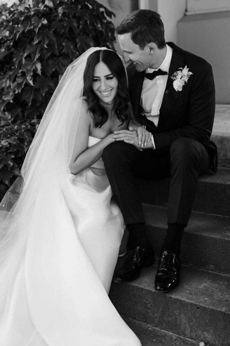 Black and white portrait of a bride and groom seated on stone steps
