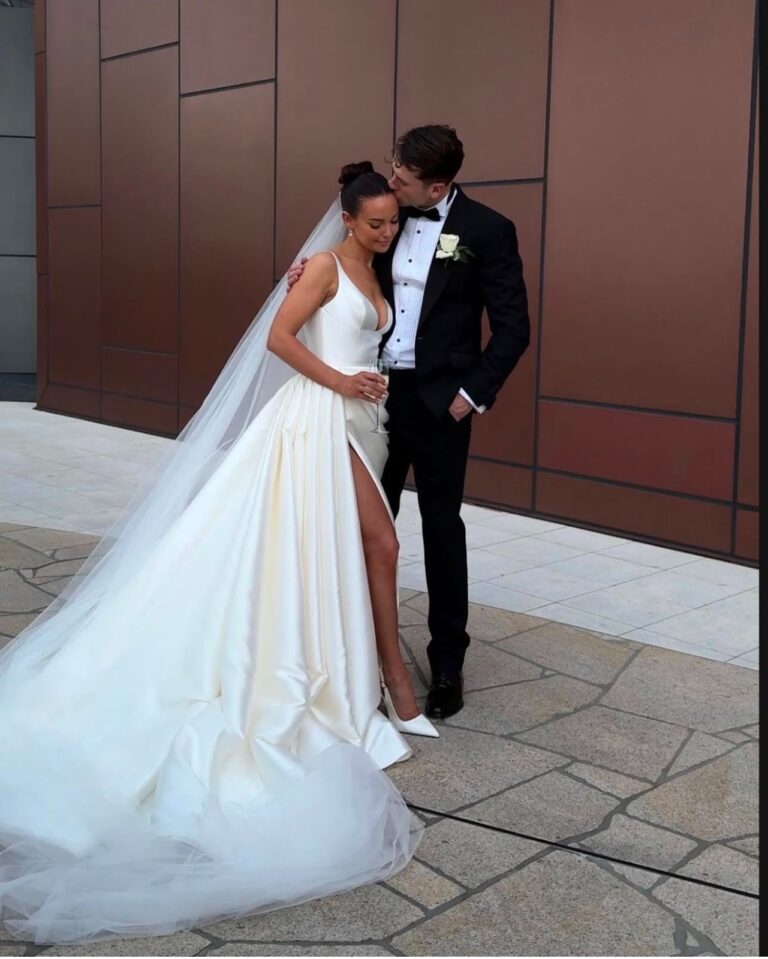 Bride and groom kissing beside a copper wall, her veil trailing behind