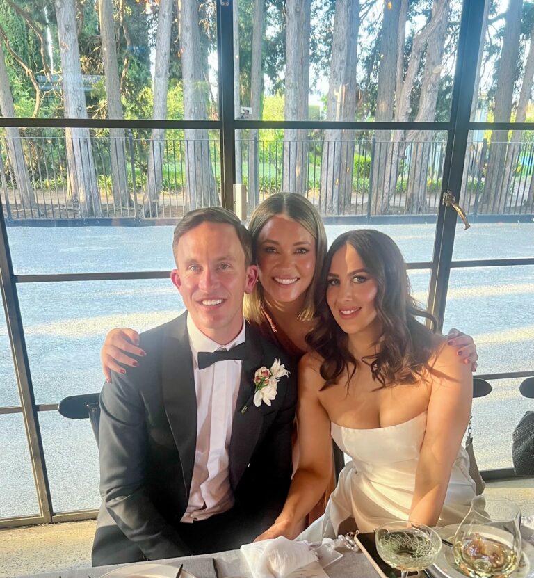 Bride and groom seated with a guest at their wedding reception